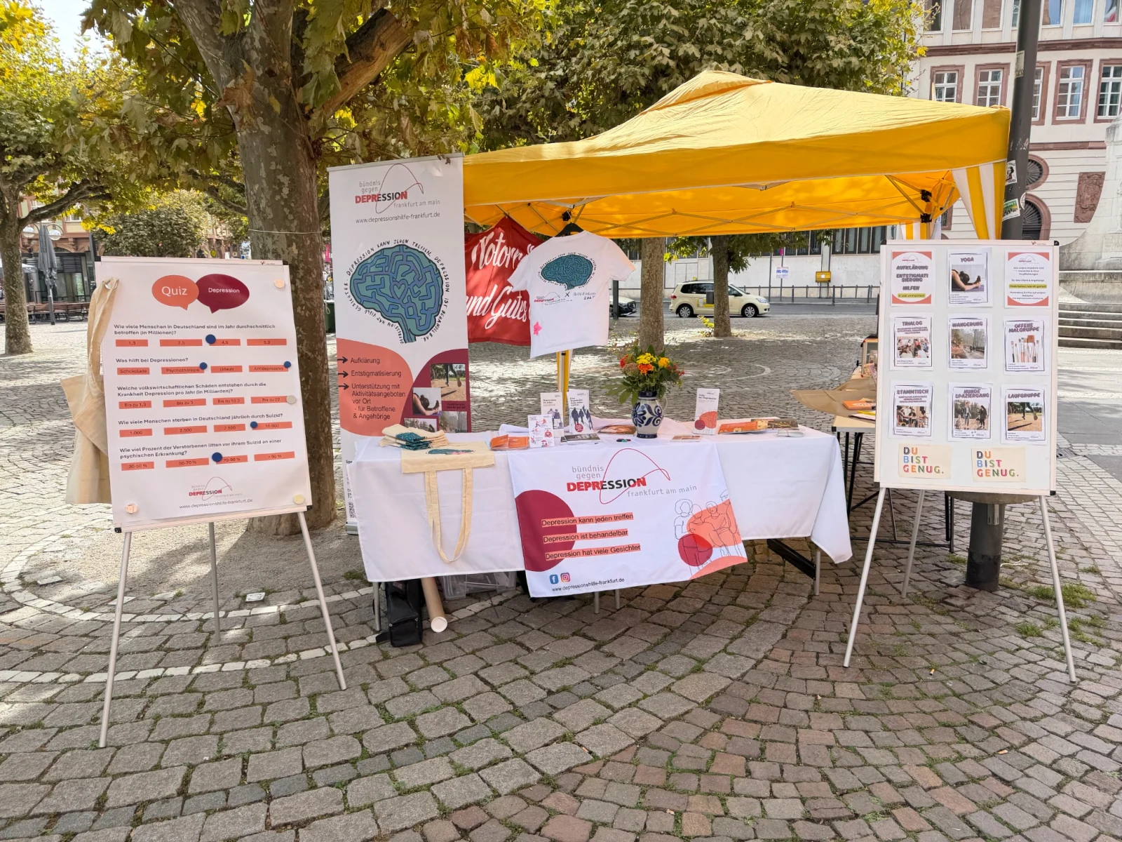 Informationsstand des Frankfurter Bündnisses gegen Depression mit gelbem Pavillon, einem Depressionsquiz und Tafeln zu den Angeboten
